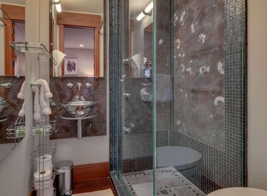 Experience luxury in this modern bathroom featuring a sleek glass-enclosed shower with unique fossil-patterned marble walls.