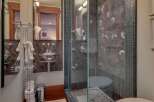 Experience luxury in this modern bathroom featuring a sleek glass-enclosed shower with unique fossil-patterned marble walls.