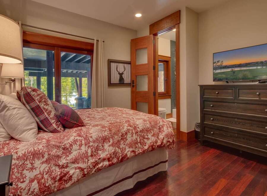 Experience rustic charm in this inviting bedroom featuring a comfortable bed with a red and white toile duvet and plaid accent pillows.