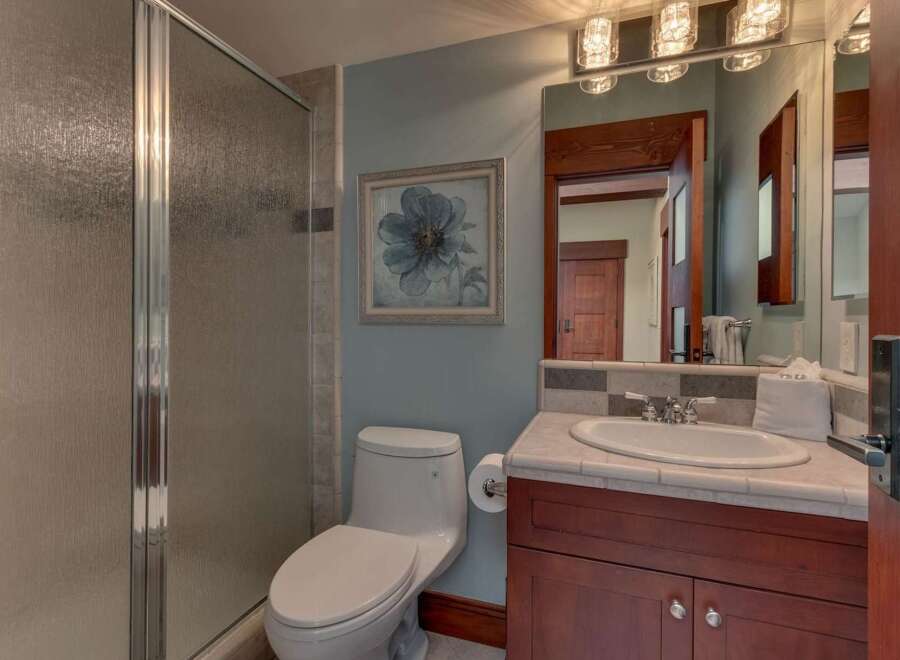 This bathroom features a sleek glass-enclosed shower and a modern toilet, complemented by a vanity with a granite countertop and a large, ornate mirror.