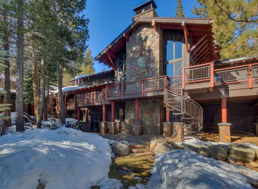 Experience luxury mountain living in this stunning stone and wood home, nestled amongst tall pine trees and surrounded by snow-covered grounds.