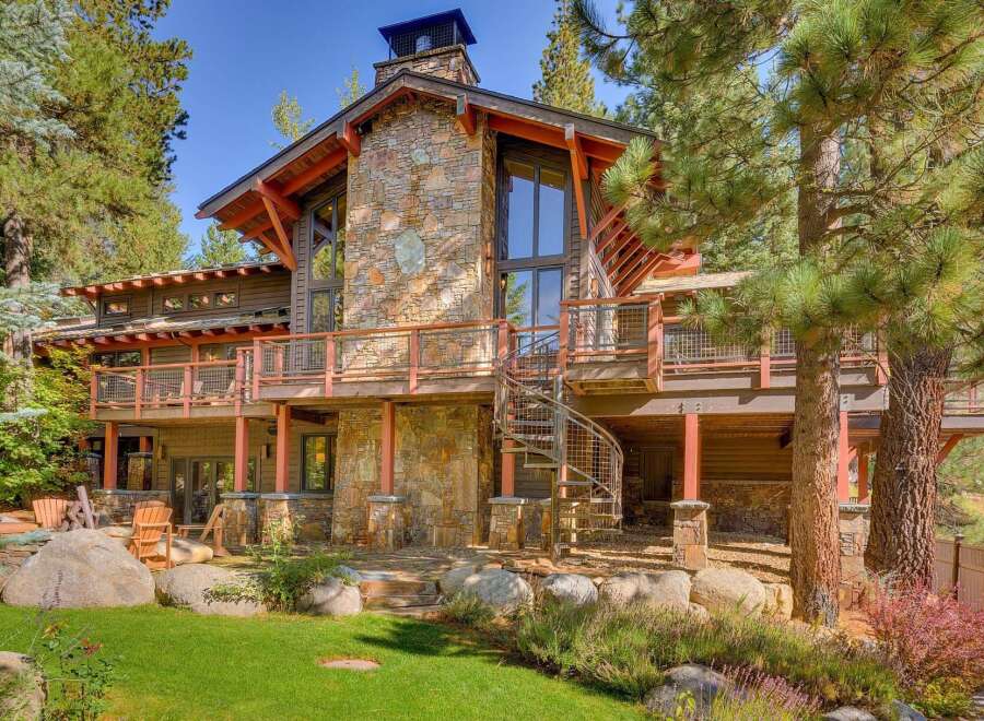 Experience luxury mountain living in this stunning timber-frame home, featuring a striking stone facade and expansive decks perfect for enjoying the surrounding pine forest.