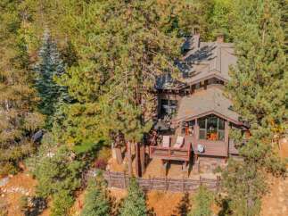 Nestled amidst towering pine trees, this charming mountain home offers a serene retreat with its expansive wooden deck, perfect for enjoying the crisp air and natural surroundings.