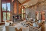 Experience rustic luxury in this stunning great room, featuring a grand stone fireplace and soaring vaulted ceilings with exposed wooden beams.