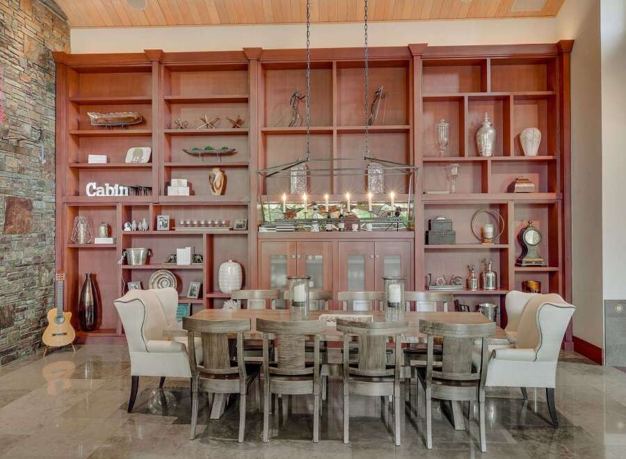 Experience rustic elegance in this spacious dining room, featuring a grand wooden bookshelf filled with decorative items and a charming 'Cabin' sign.