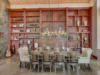 Experience rustic elegance in this spacious dining room, featuring a grand wooden bookshelf filled with decorative items and a charming 'Cabin' sign.
