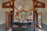 Experience luxury mountain living in this stunning kitchen, featuring a vaulted wood-paneled ceiling with exposed beams and a dramatic floor-to-ceiling window overlooking a lush forest.