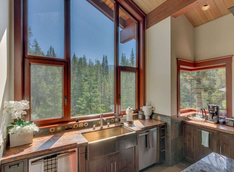 Experience breathtaking natural beauty from this stunning kitchen, featuring a large farmhouse sink and expansive windows that frame a panoramic view of a lush forest.