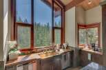 Experience breathtaking natural beauty from this stunning kitchen, featuring a large farmhouse sink and expansive windows that frame a panoramic view of a lush forest.