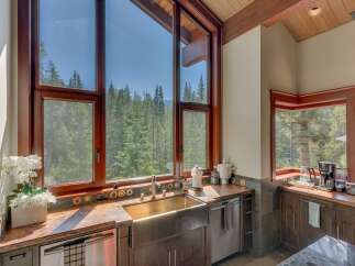 Experience breathtaking natural beauty from this stunning kitchen, featuring a large farmhouse sink and expansive windows that frame a panoramic view of a lush forest.