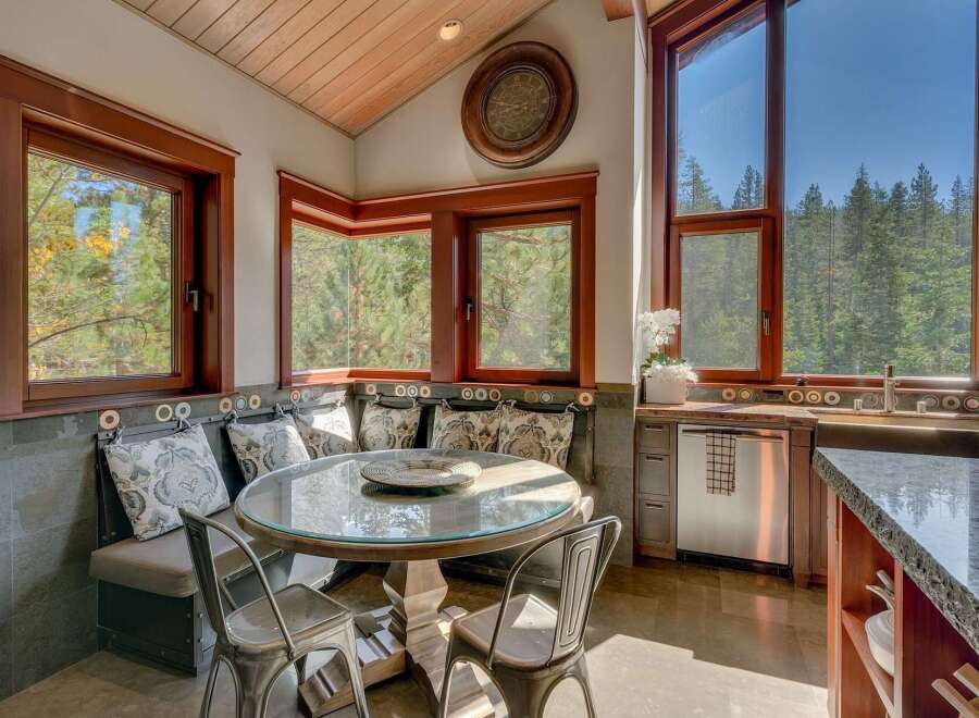 Enjoy breathtaking forest views from this charming kitchen nook, complete with a built-in banquette and a round glass-top table perfect for intimate meals.
