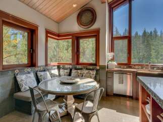 Enjoy breathtaking forest views from this charming kitchen nook, complete with a built-in banquette and a round glass-top table perfect for intimate meals.