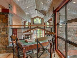 Experience rustic luxury in this stunning mountain home, featuring exposed wooden beams and a grand stone fireplace.