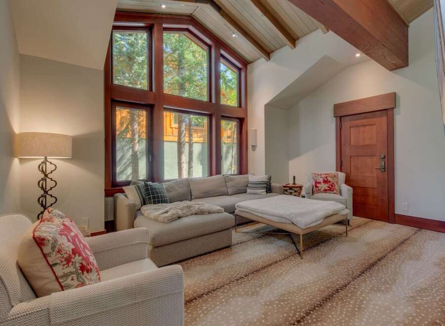 Experience luxurious mountain living in this stunning living room, featuring a grand vaulted ceiling with exposed wooden beams and a massive wall of windows that flood the space with natural light and offer breathtaking forest views.
