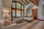 Experience luxurious mountain living in this stunning living room, featuring a grand vaulted ceiling with exposed wooden beams and a massive wall of windows that flood the space with natural light and offer breathtaking forest views.