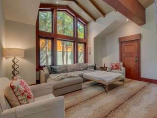 Experience luxurious mountain living in this stunning living room, featuring a grand vaulted ceiling with exposed wooden beams and a massive wall of windows that flood the space with natural light and offer breathtaking forest views.