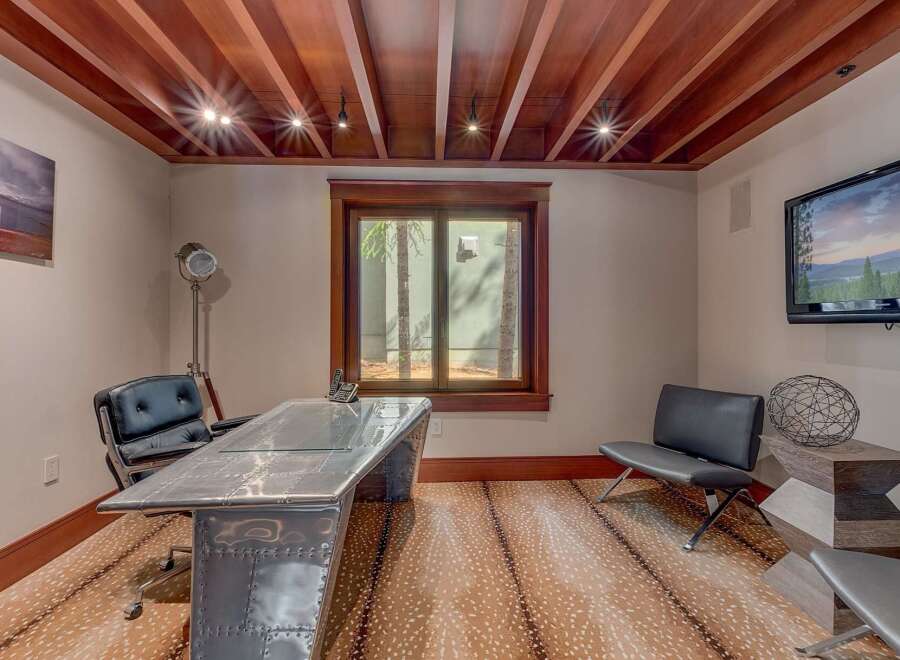 This home office features a unique, industrial-style desk with a metallic finish and glass top, complemented by a sleek black leather executive chair.