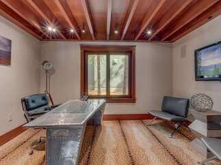 This home office features a unique, industrial-style desk with a metallic finish and glass top, complemented by a sleek black leather executive chair.