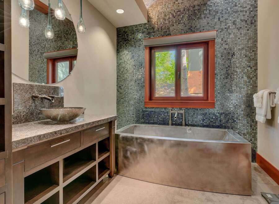 Experience luxury in this modern bathroom featuring a sleek, stainless steel soaking tub positioned beneath a window with a scenic view.