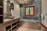 Experience luxury in this modern bathroom featuring a sleek, stainless steel soaking tub positioned beneath a window with a scenic view.