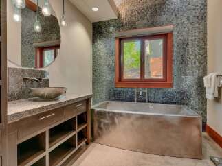 Experience luxury in this modern bathroom featuring a sleek, stainless steel soaking tub positioned beneath a window with a scenic view.
