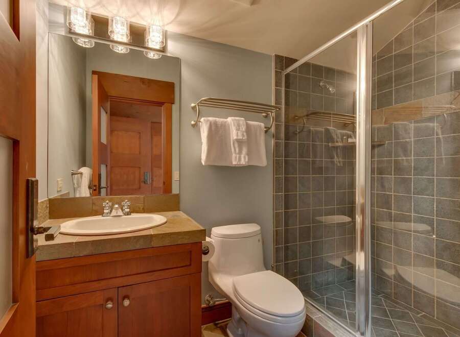 This bathroom features a modern vanity with a stone countertop and a sleek undermount sink, complemented by a large mirror with stylish vanity lighting.