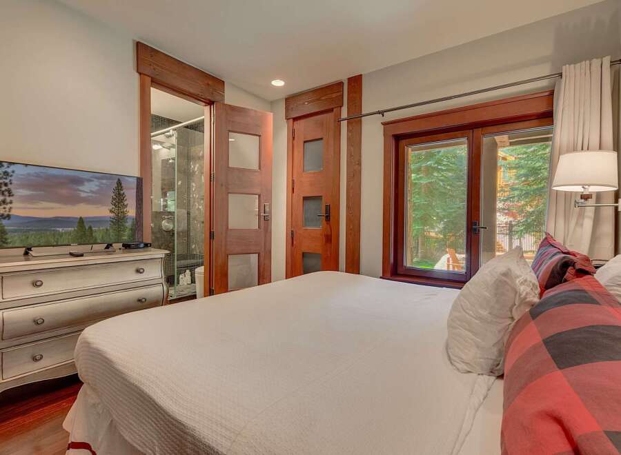 Experience ultimate comfort in this beautifully appointed bedroom, featuring a large flat-screen TV mounted on an antique dresser and direct access to a luxurious en-suite bathroom.