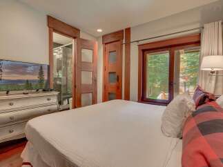 Experience ultimate comfort in this beautifully appointed bedroom, featuring a large flat-screen TV mounted on an antique dresser and direct access to a luxurious en-suite bathroom.