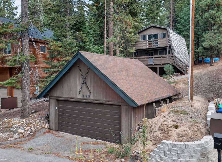 Nestled amidst tall pine trees, this charming mountain property features a rustic wooden exterior and a spacious two-car garage adorned with decorative skis and the house number 1369.