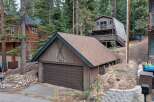 Nestled amidst tall pine trees, this charming mountain property features a rustic wooden exterior and a spacious two-car garage adorned with decorative skis and the house number 1369.