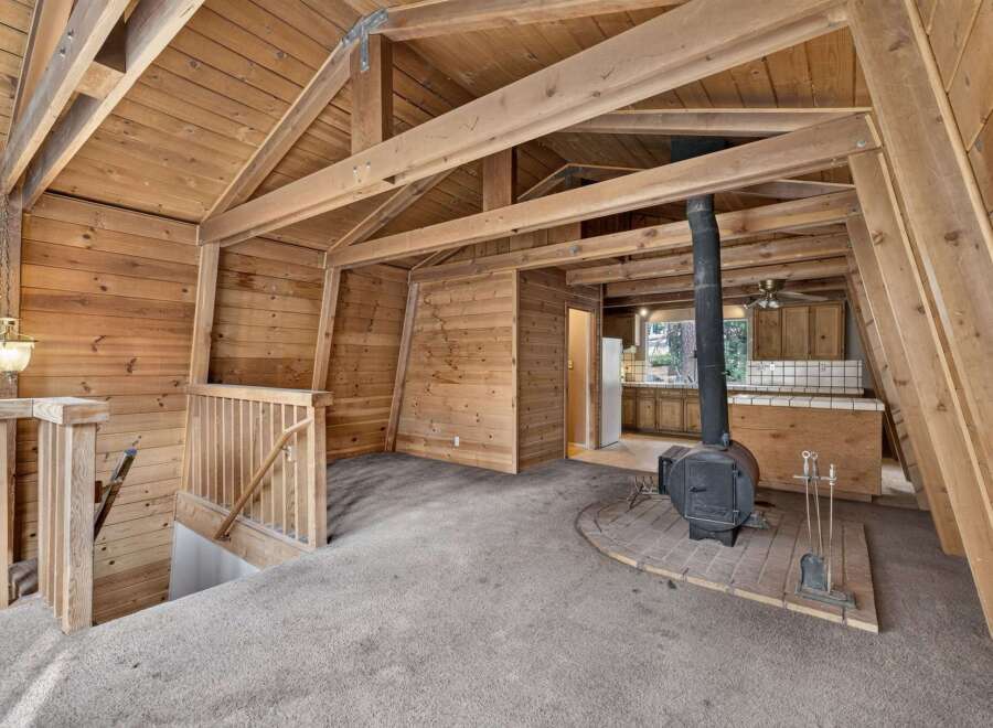 Experience rustic charm in this A-frame cabin featuring a cozy living area with a wood-burning stove and exposed wooden beams.