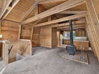 Experience rustic charm in this A-frame cabin featuring a cozy living area with a wood-burning stove and exposed wooden beams.