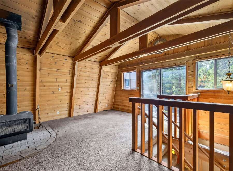 Cozy up by the wood-burning stove in this charming rustic living room, featuring exposed wooden beams and a vaulted ceiling.