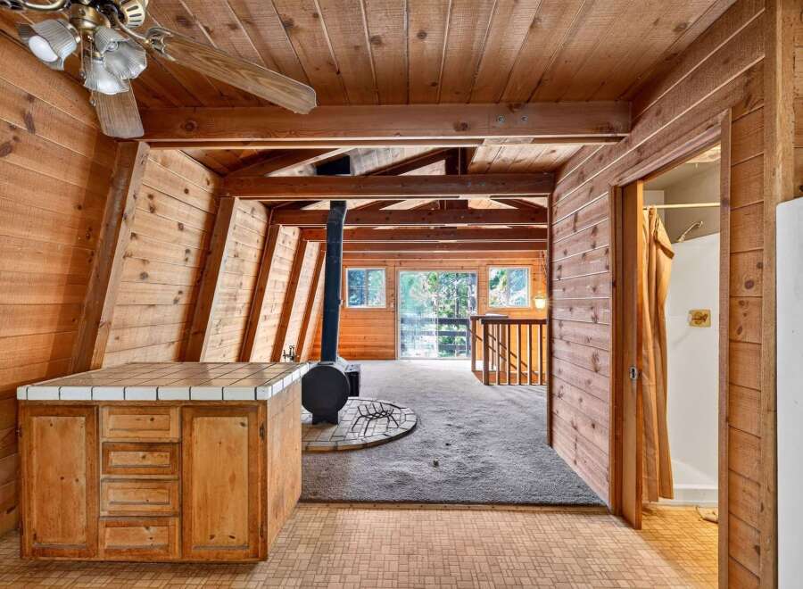 Experience rustic charm in this A-frame cabin featuring a cozy wood-paneled interior and a central wood-burning stove.