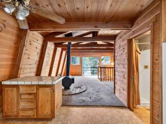 Experience rustic charm in this A-frame cabin featuring a cozy wood-paneled interior and a central wood-burning stove.