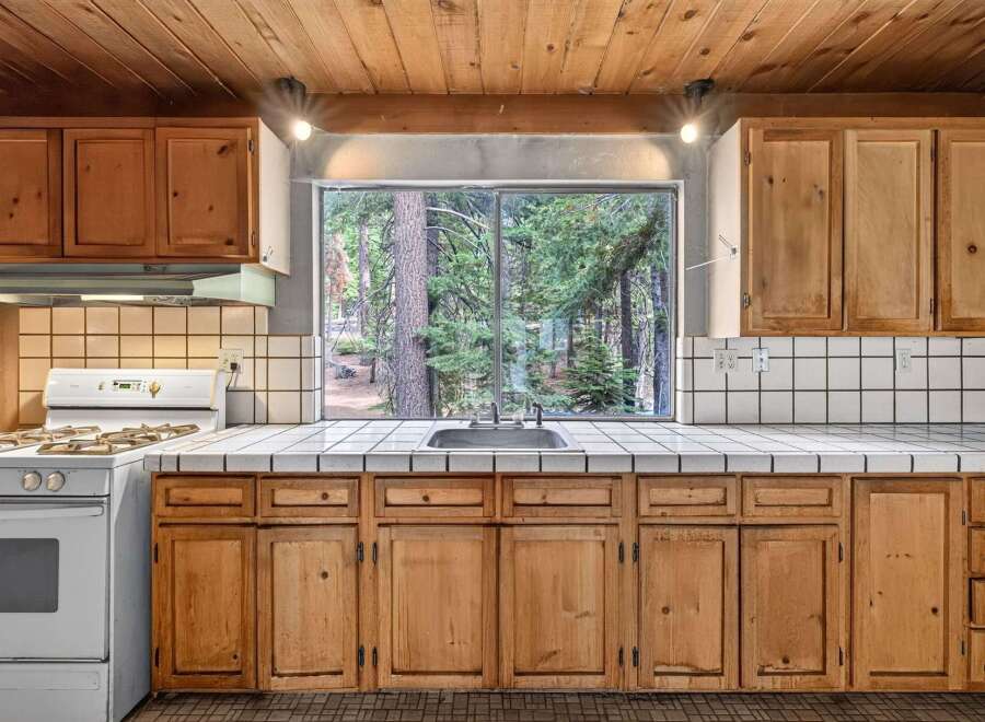 Enjoy cooking with a view in this charming kitchen featuring a large window overlooking a serene forest.