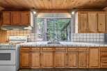 Enjoy cooking with a view in this charming kitchen featuring a large window overlooking a serene forest.