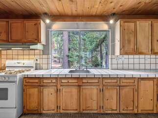 Enjoy cooking with a view in this charming kitchen featuring a large window overlooking a serene forest.