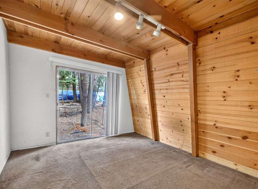 Experience rustic charm in this cozy room featuring warm wood paneling and a sloped wooden ceiling with exposed beams.