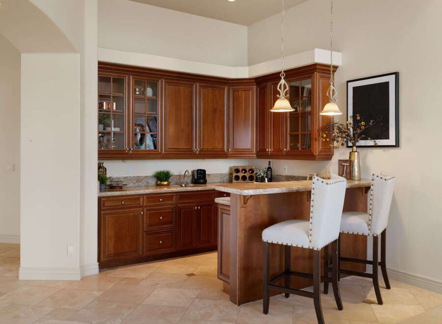 This elegant wet bar features rich cherry wood cabinetry with glass-front upper cabinets, perfect for displaying glassware.