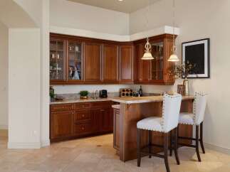 This elegant wet bar features rich cherry wood cabinetry with glass-front upper cabinets, perfect for displaying glassware.