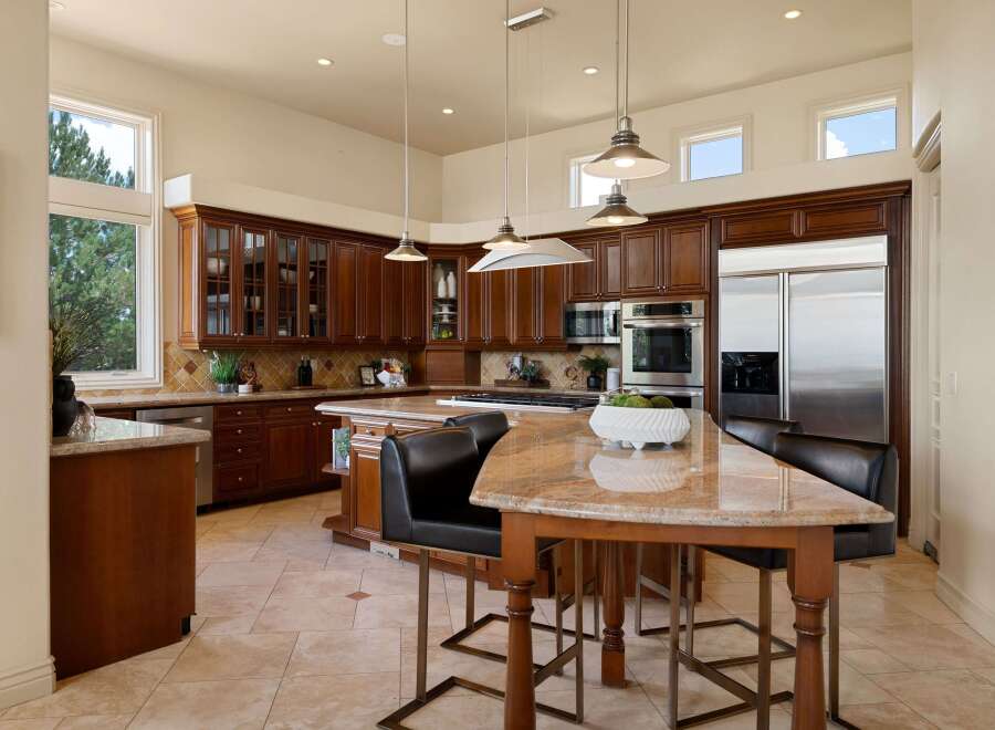 This spacious kitchen boasts rich cherry wood cabinetry with glass-fronted upper cabinets, complemented by granite countertops and a large island with a granite surface.