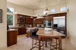 This spacious kitchen boasts rich cherry wood cabinetry with glass-fronted upper cabinets, complemented by granite countertops and a large island with a granite surface.