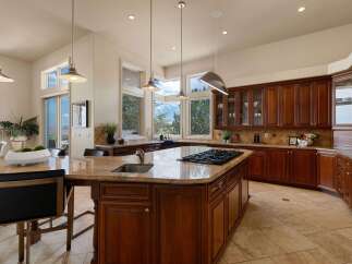 Experience luxury in this spacious kitchen featuring rich cherry wood cabinetry and a large granite island with a built-in gas range.
