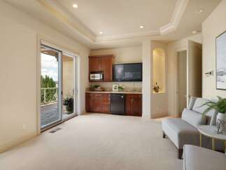 This spacious room features a built-in wet bar with rich wood cabinetry, a microwave, and a mini-fridge, perfect for entertaining.
