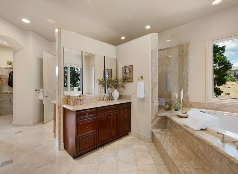 Indulge in luxury in this spacious master bathroom, featuring a large soaking tub with a marble surround and a separate glass-enclosed shower.
