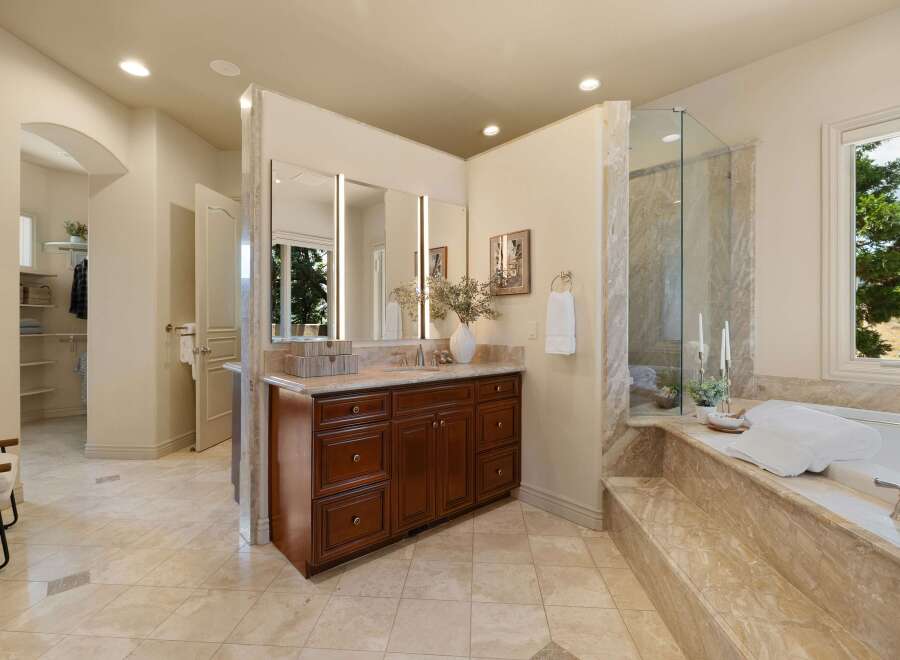 This luxurious bathroom features a spacious vanity with a marble countertop and dark wood cabinetry, complemented by a large mirror with integrated lighting.