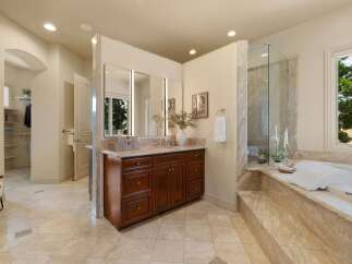 This luxurious bathroom features a spacious vanity with a marble countertop and dark wood cabinetry, complemented by a large mirror with integrated lighting.