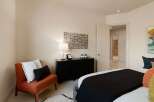 This inviting bedroom features a stylish orange accent chair with decorative pillows, complemented by a sleek black dresser adorned with a modern lamp and minimalist decor.