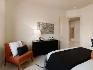 This inviting bedroom features a stylish orange accent chair with decorative pillows, complemented by a sleek black dresser adorned with a modern lamp and minimalist decor.